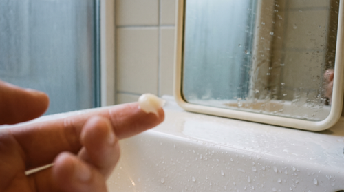 A pea-sized dab of tallow balm on a fingertip beside a wet sink, how to use beef tallow balm on damp skin