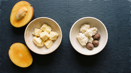 Mango butter and shea butter in two bowls side by side on slate