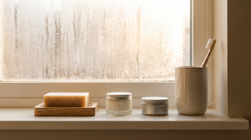 Soap bar, cream jar and a tin lined up on a bathroom vanity, a three-step morning skincare routine