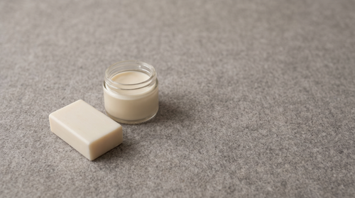 One soap bar and one jar of cream on grey felt with lots of empty space, natural skincare for sensitive skin