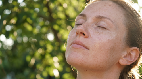 Close portrait of a freckled, fair-skinned woman in dappled afternoon sun with a thin sheer layer of sunscreen on her cheeks