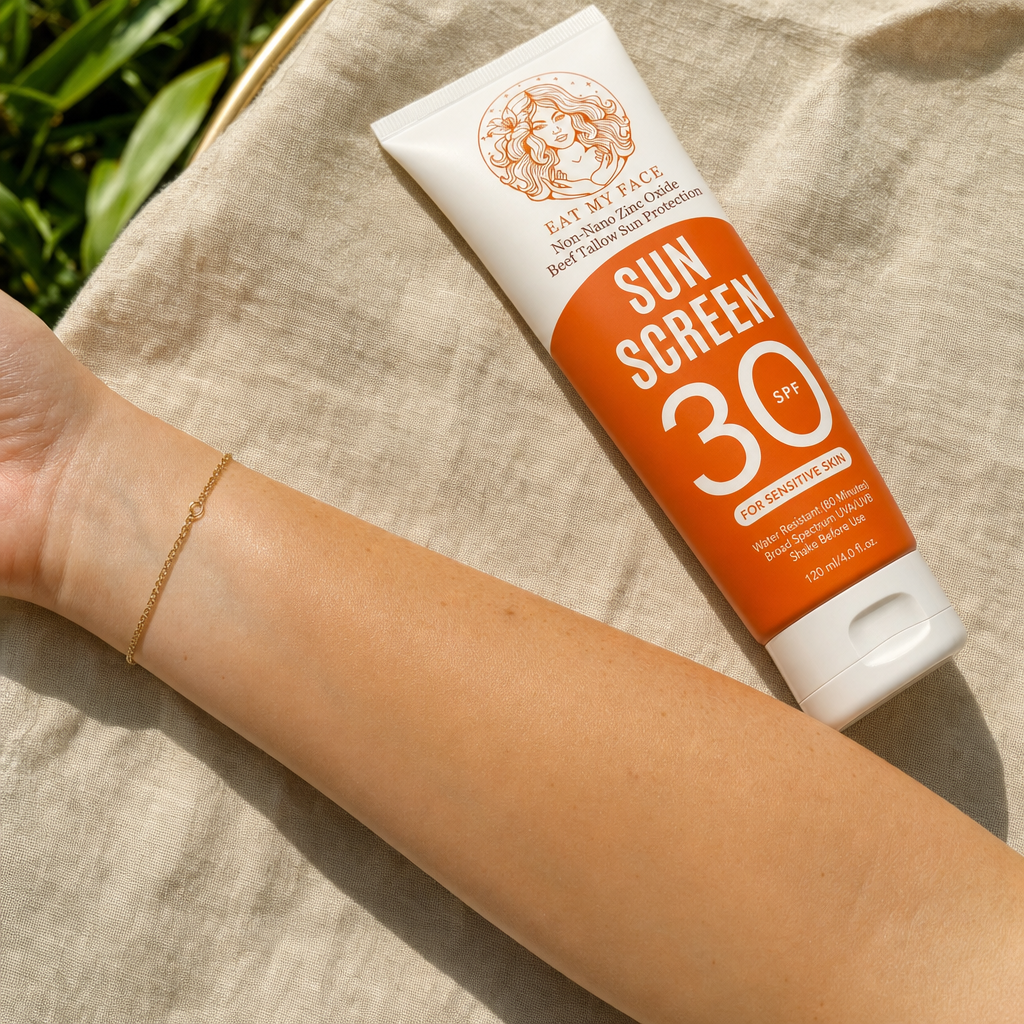 Eat My Face SPF 30 mineral sunscreen tube held above a fully blended, no-white-cast swatch on an inner forearm — proof shot showing the slight warm tint blends naturally without chalky residue.